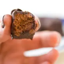 A hand holds a bite-sized vegan 3 Muskateers Bars with a bite taken out of it.