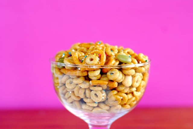 A glass bowl of glazed cereal and goodies in front of a pink and red background.