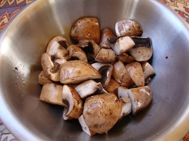 Portobello mushroom pieces marinating in a metal bowl.