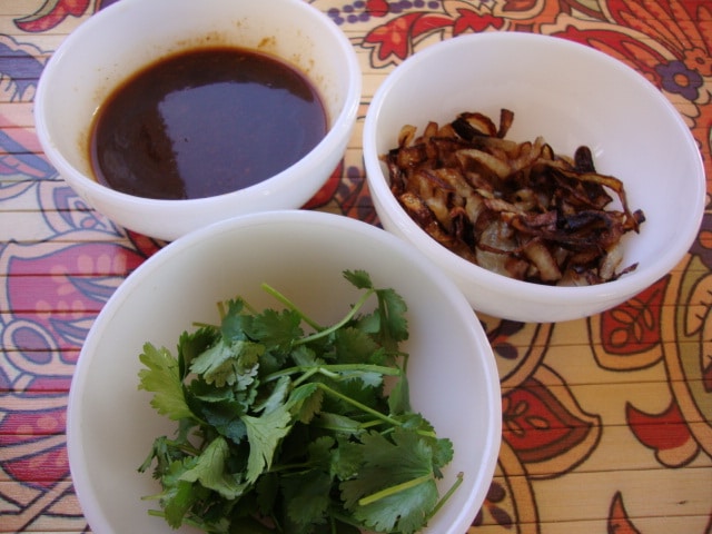 Three bowls contain a hoisin sauce, caramelized onions, and sprigs of cilantro.