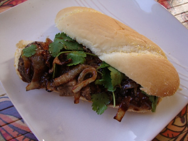 A hoagie bun holds mushroom pieces, caramelized onions, and greens.