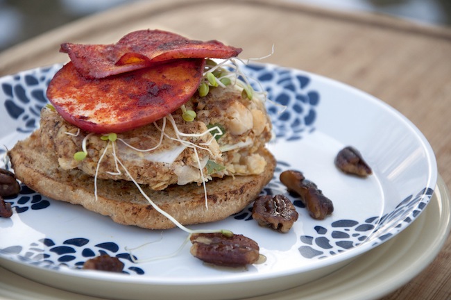 A sandwich with smoked apple and sprouts on a plate with pecans.