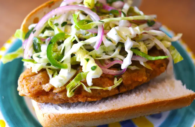 A vegan fried chicken sandwich with slaw and sliced red onions on top.