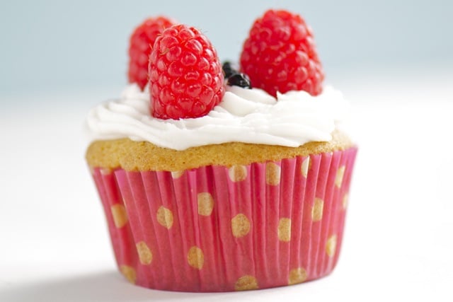 A patriotic cupcake with raspberries on top sits on a white countertop.
