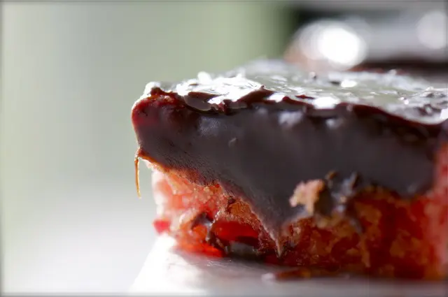 A straweberry cake topped with chocolate fudge icing is backlit by the morning sun.