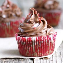 Three Chocolate cherry cupcakes sit on a napkin on a wooden table.