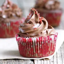 Three Chocolate cherry cupcakes sit on a napkin on a wooden table.