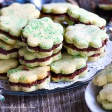 A tray of several shamrock cookies sits next to a bowl of green sprinkles.