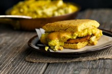 A gluten-free sweet potato biscuit sandwich sits on a plate on a wooden table with another sandwich behind it.