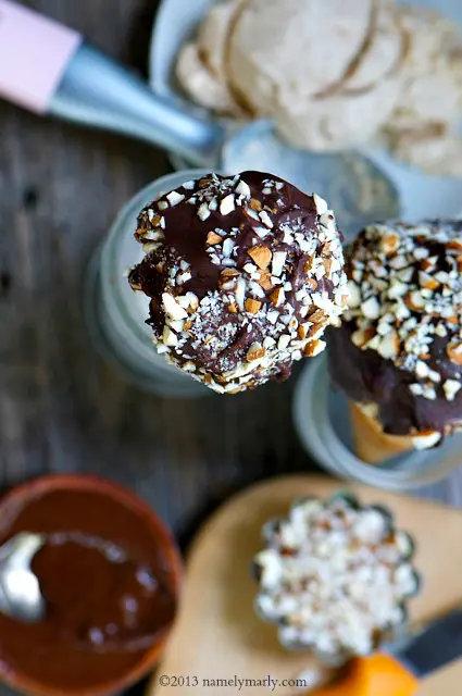 Looking down on frozen drumsticks with chopped nuts and melted chocolate beside them.