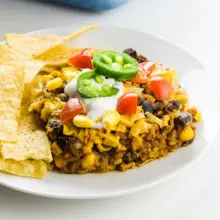 A closeup of a slice of a Mexican casserole on a plate surrounded by tortilla chips.