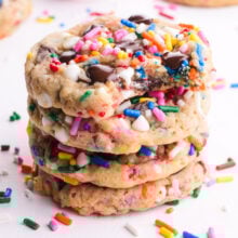A stack of Vegan Chocolate Chip Sprinkle Cookies. The top cookie has a bite taken out and colorful sprinkles are scattered around.