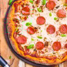 Looking down on a vegan pizza on a wooden counter with a pizza cuter next to it.