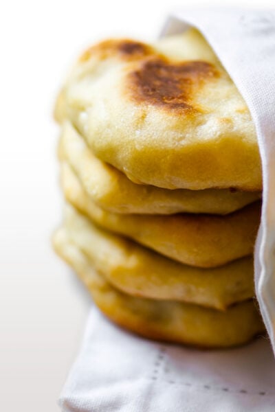 A stack of baked Naan Bread is nestled in a white kitchen cloth napkin.
