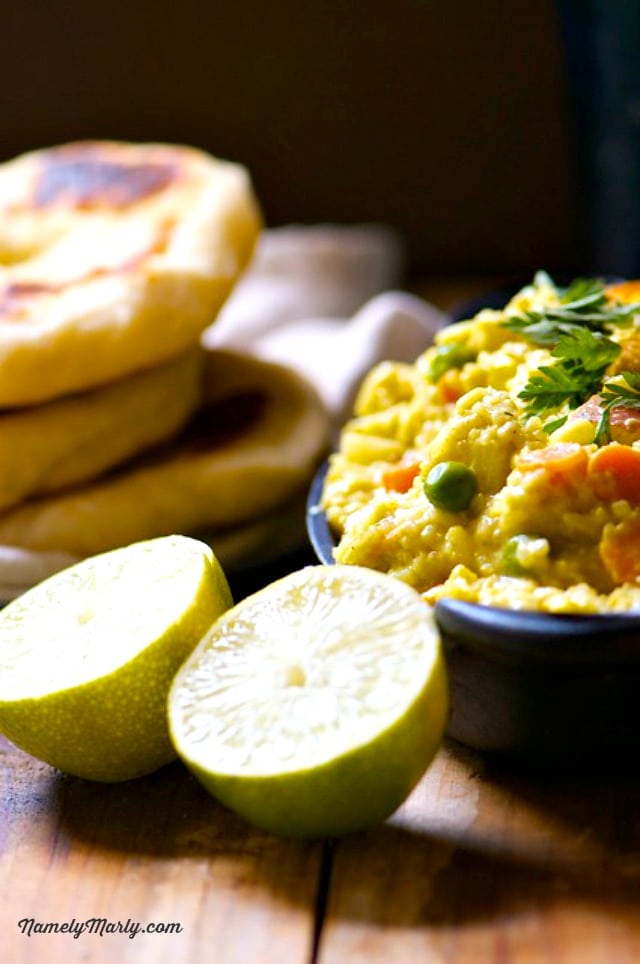 A dish of chickpea coconut curry sits next to naan bread and limes cut in half.