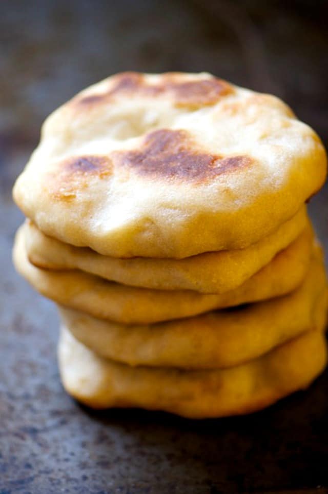 I stack of naan bread shows the top one with bits of golden brown crust on top.
