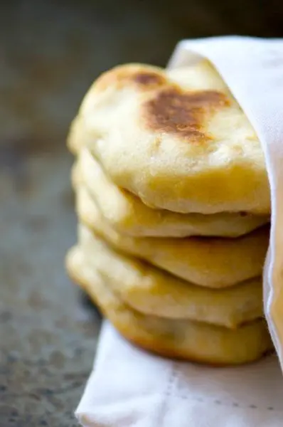 A stack of baked Naan Bread is nestled in a white kitchen cloth napkin.