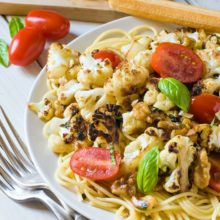 A plate holds pasta topped with cauliflower and walnuts and chopped tomatoes.