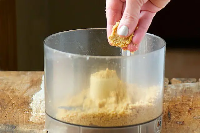 A hand reaches in and shows how pressing the graham cracker crust should stick together.