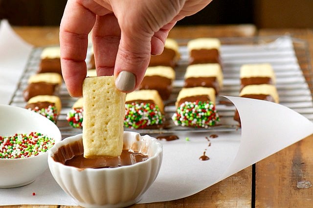 A hand holds a shortbread cookie preparing to dip it into a bowl of melted chocolates. 