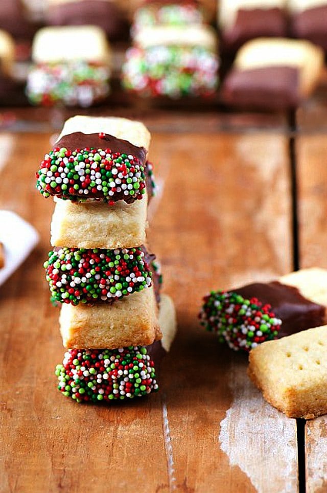 Several Chocolate Dipped Shortbread Cookies are stacked tall, next to more cookies.