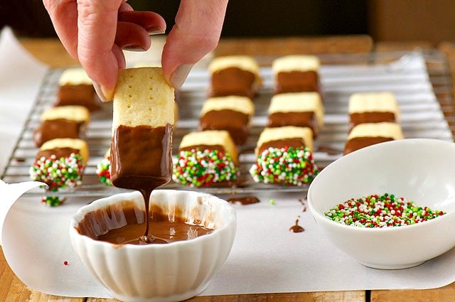 A hand pulls a shortbread cookie out of melted chocolate.