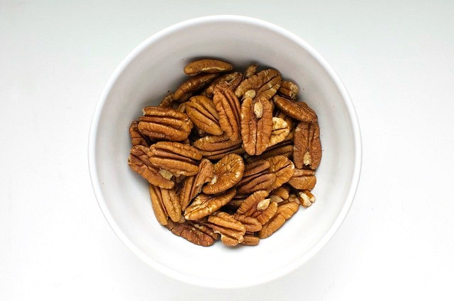 Pecans sit in a white bowl on a white counter.