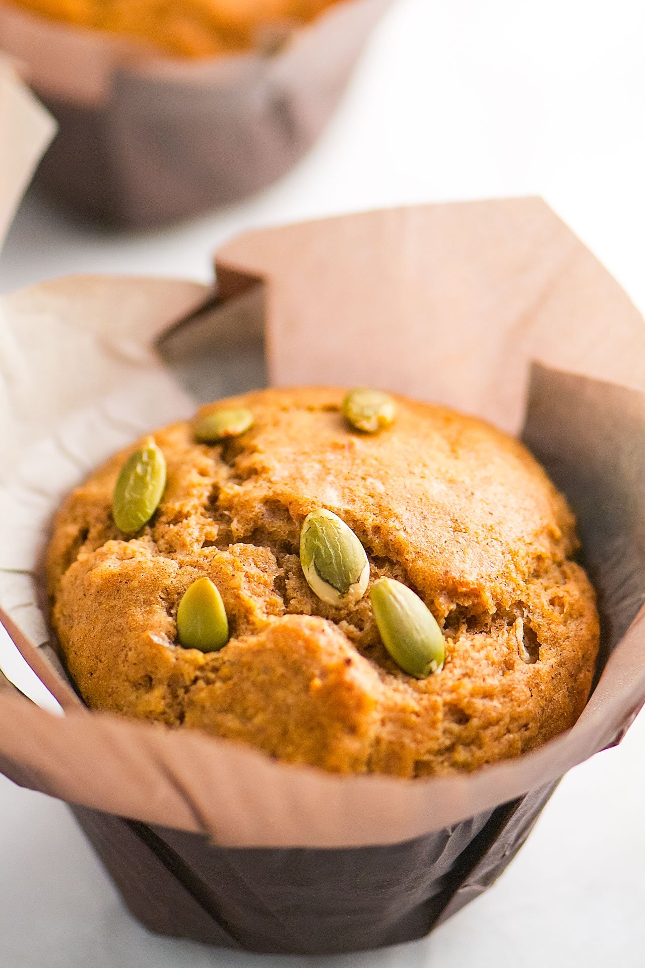 A closeup of a muffin with pumpkin seeds on top. The muffin is in a large brown paper.