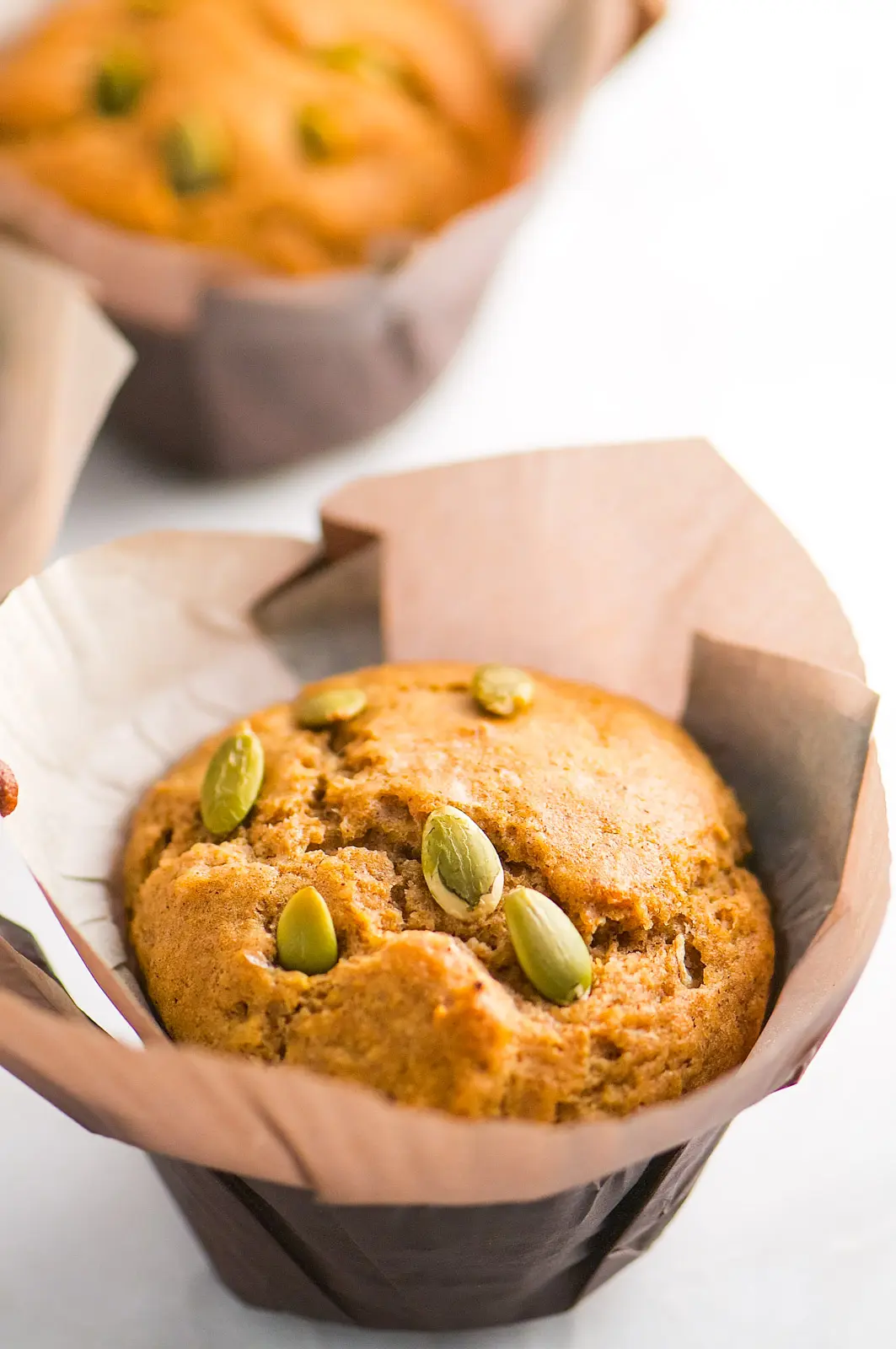 A closeup of a muffin with pumpkin seeds on top. The muffin is in a large brown paper.