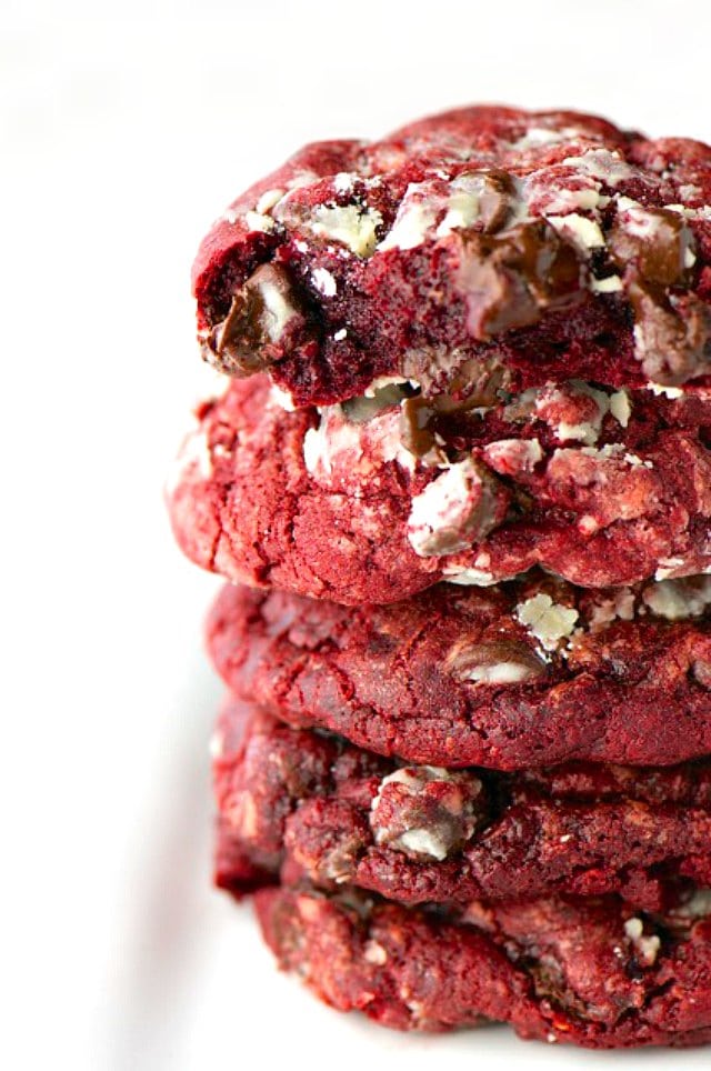 A closeup of a stack of red chocolate chip cookies. A bite has been taken out of the top one to reveal melted chocolate chips.