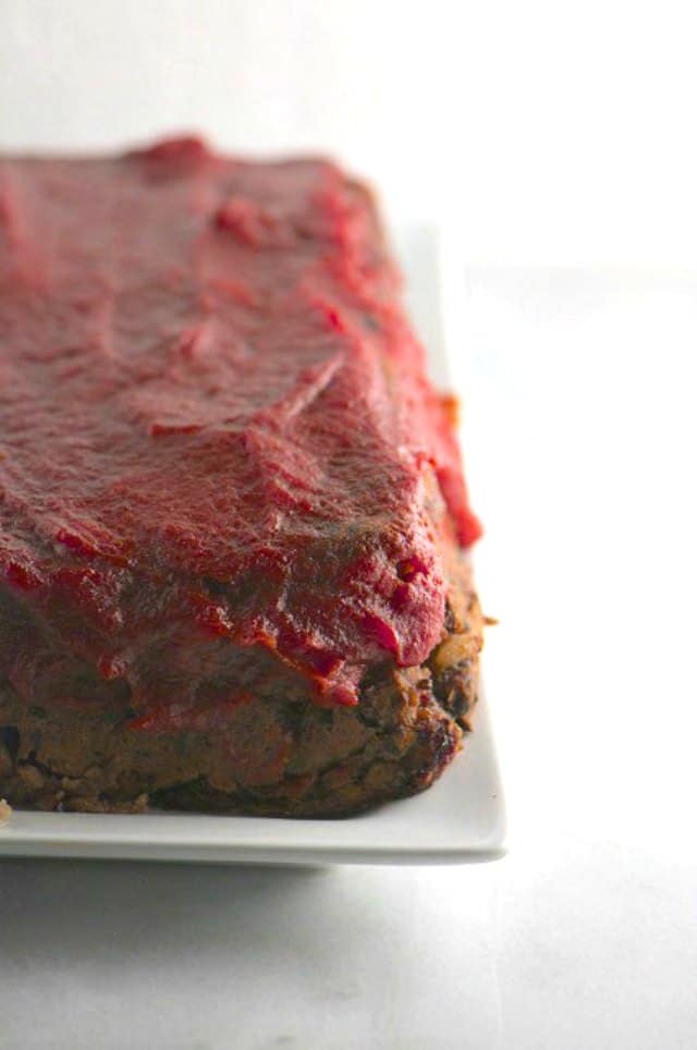 A vegan meatloaf sits on a serving dish and is topped with red sauce.