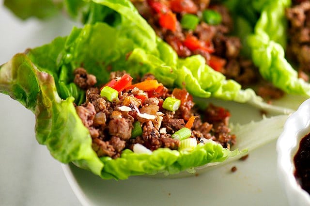 A lettuce cup is filled with a tofu mixture. It sits on a white tray next to more lettuce cups and a dipping sauce.