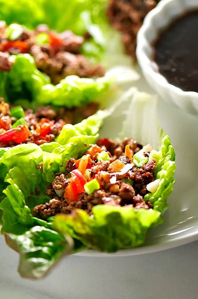 A close up of several vegetarian lettuce wraps filled with veggie filling next to a bowl of dipping sauce.