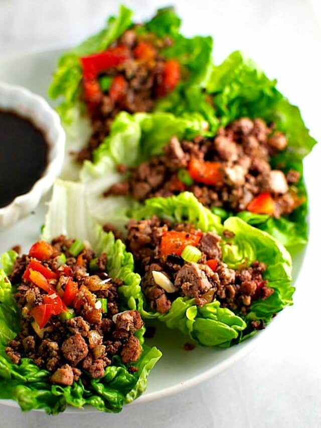 A platter of lettuce wraps filled with veggie filling and sitting next to a bowl of dipping sauce.