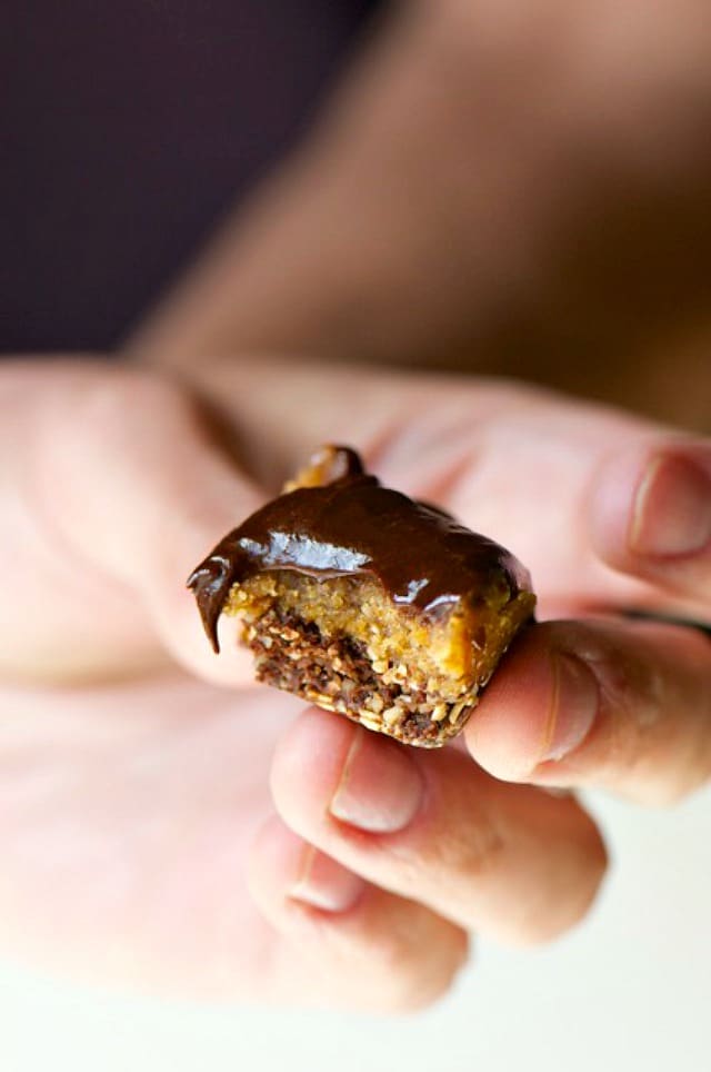 A hand holds a half-eat chocolate peanut butter cup with melty chocolate on top.