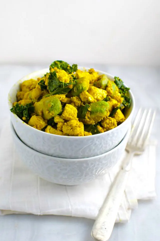 A tofu breakfast bowl with scrambled tofu bits of kale and avocado sit next to a fork.
