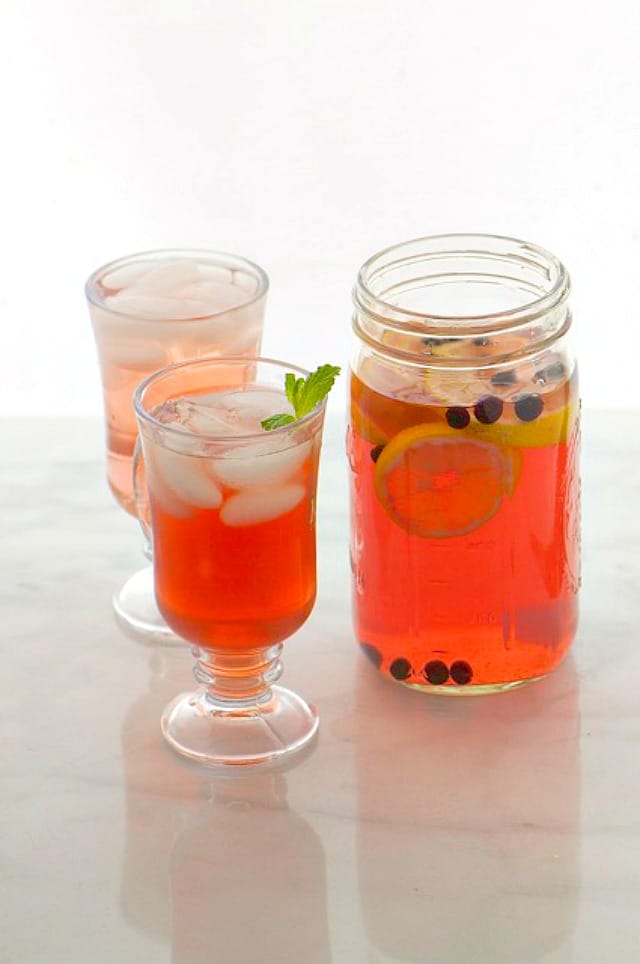 Two glasses hold fruit punch, ice, and mint sprigs. A mason jar is next to it with more fruit punch.