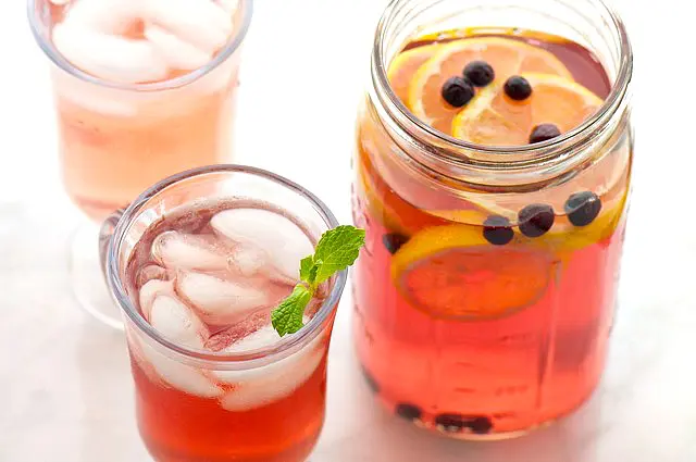 Looking down on two glasses and a mason jar with fruit punch. The jar holds fresh berries and orange slices.