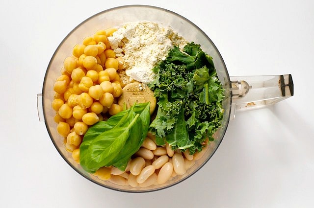 A food processor bowl holds beans, kale, basil, and flour.