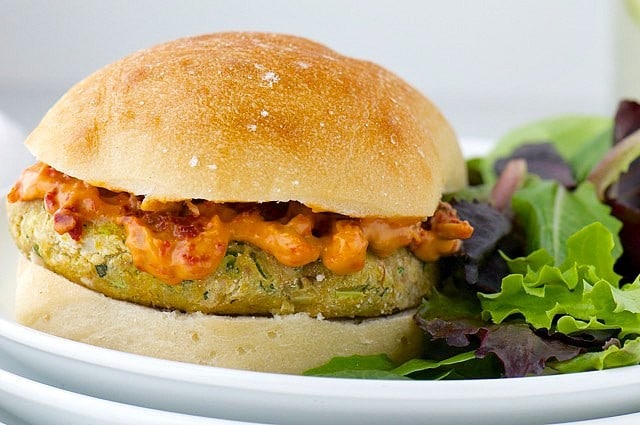 A pesto veggie burger on a bun sits next to field greens.