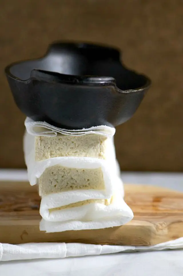 Blocks of tofu are wrapped with paper towels and topped with a small, but heavy iron dish.