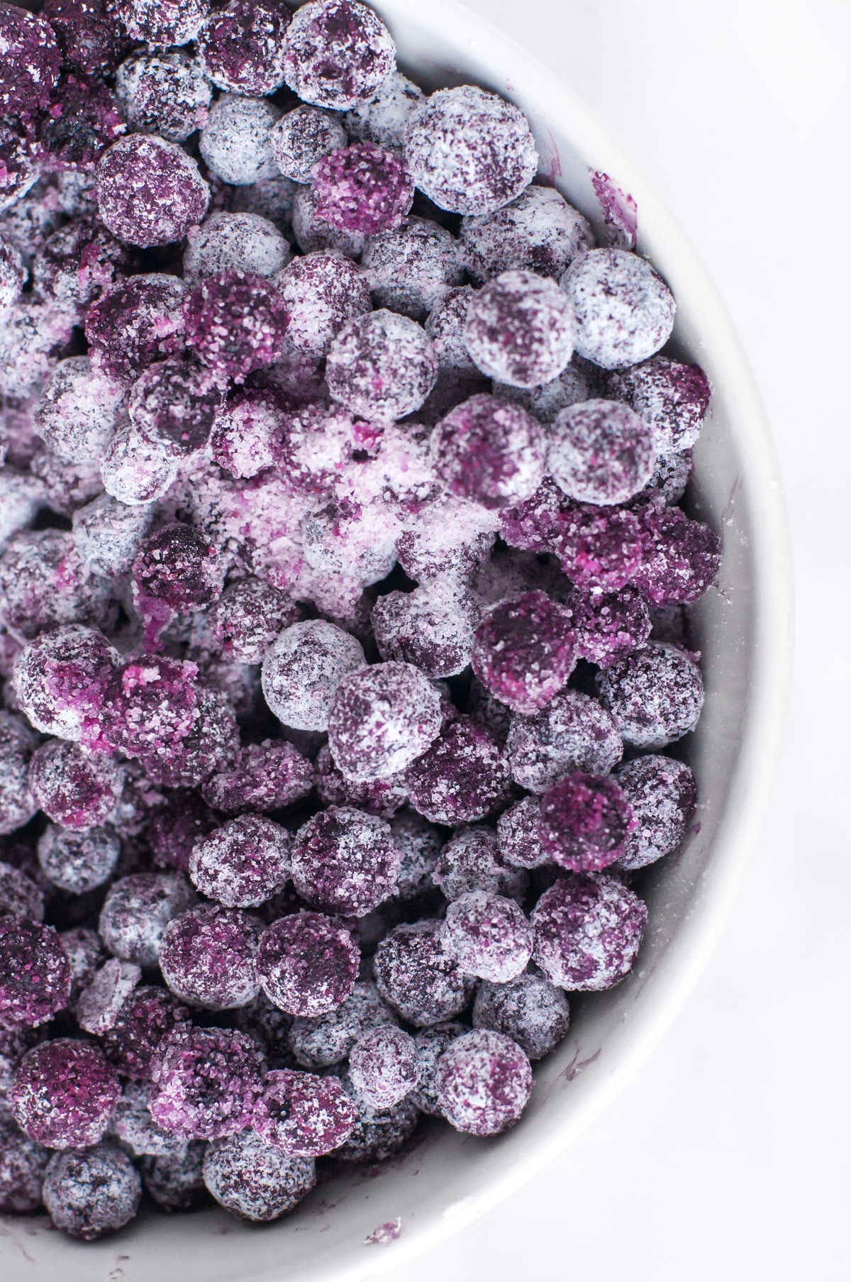 Blueberries have been coated with flour and are sitting in a white bowl.