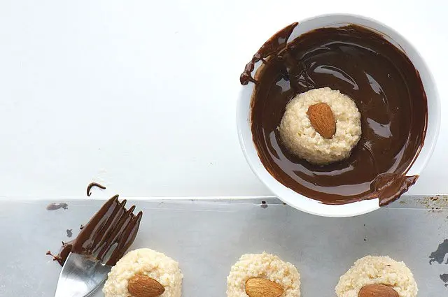 A coconut ball topped with an almond is dropped in melted chocolate to be coated.