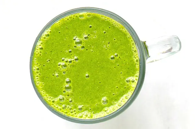 Looking down at a glass mug full of green smoothie, with lots of bubbles on the top, showing it was just freshly blended.
