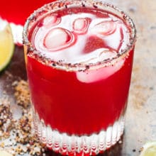 Two glasses of Hibiscus Margaritas with lime wedges around them.