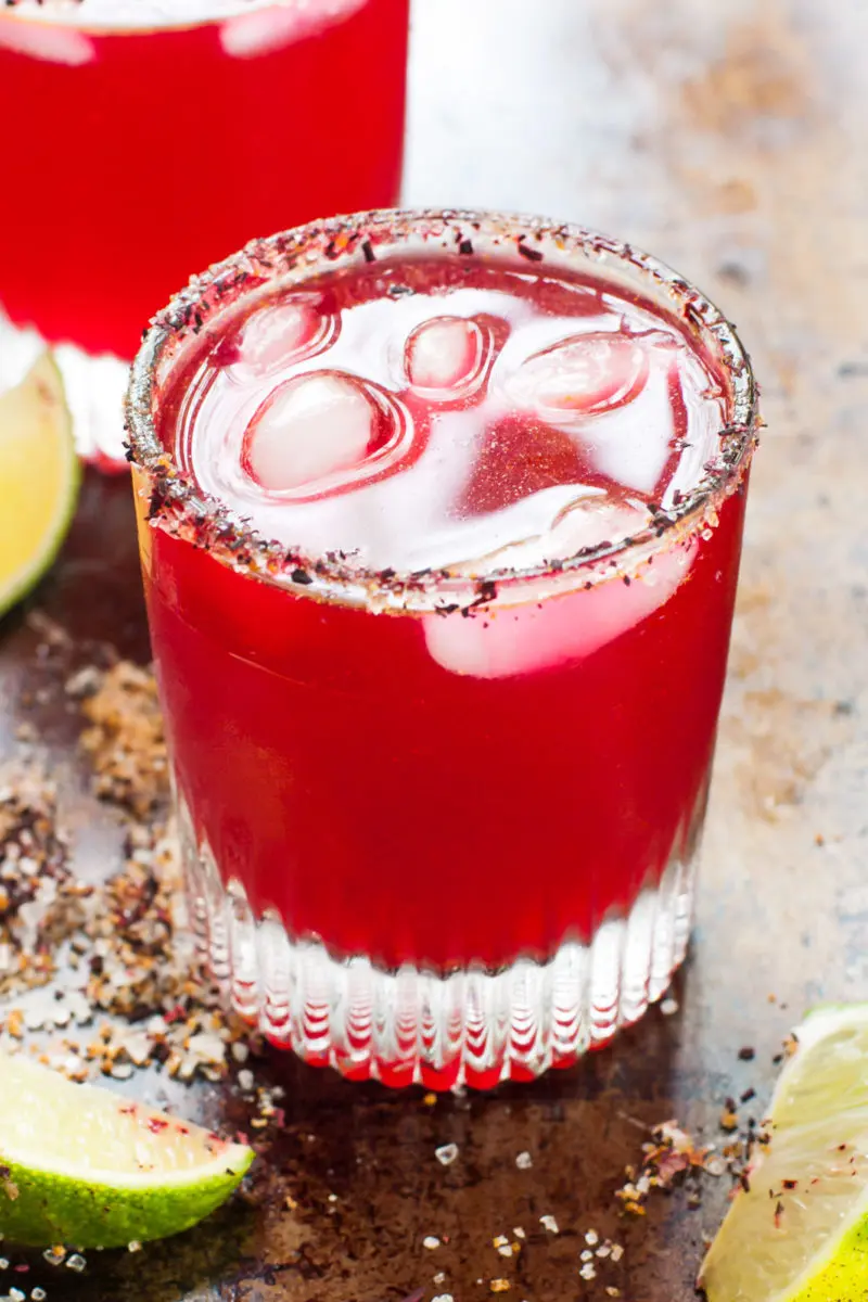 Two glasses of Hibiscus Margaritas with lime wedges around them.