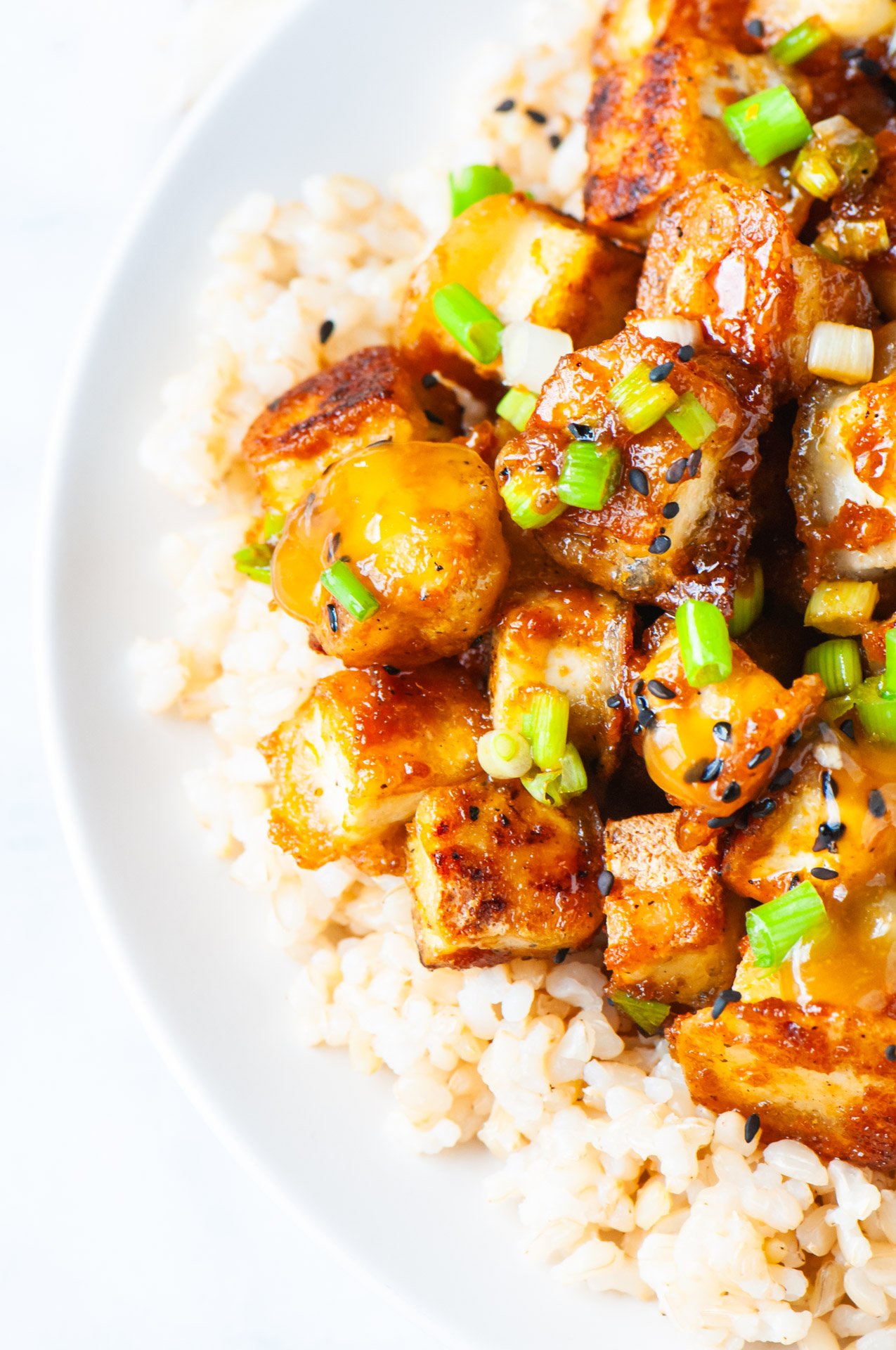 Crispy Orange Tofu on a bed of rice with sliced green onions on top.