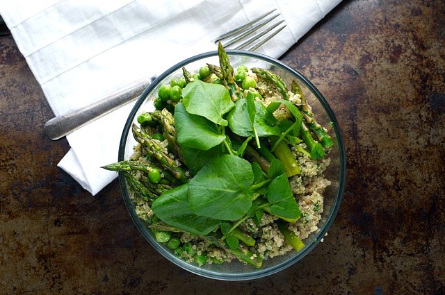 Looking down on a glass bowl with quinoa, asparagus, and fresh spinach leaves. A white dinner napkin and fork sit above it.