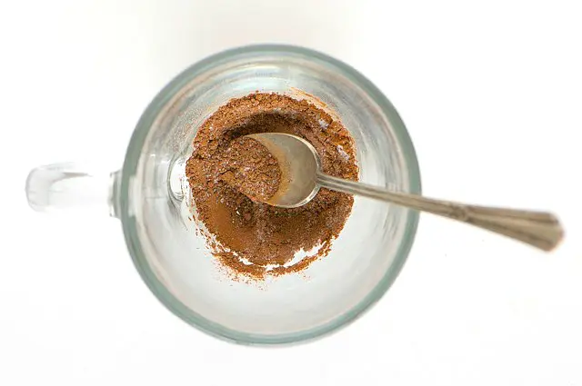 Looking down on the cocoa mix at the bottom of the glass coffee mug. A spoon is in the cup as well.