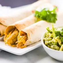 Vegan chicken taquitos are on a plate next to guacamole.